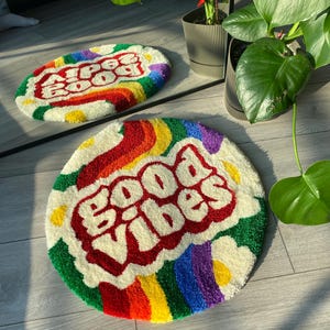 May include: Round, white, fluffy rug with a rainbow border and the words "Good Vibes" in red, outlined in white, in a retro font.