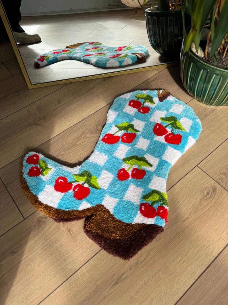 May include: A blue and white checkered bath mat shaped like a cowboy boot with red cherries on it.