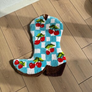 May include: A blue and white checkered boot rug with red cherries. The rug is made of a soft, fluffy material and has a brown leather-like heel.