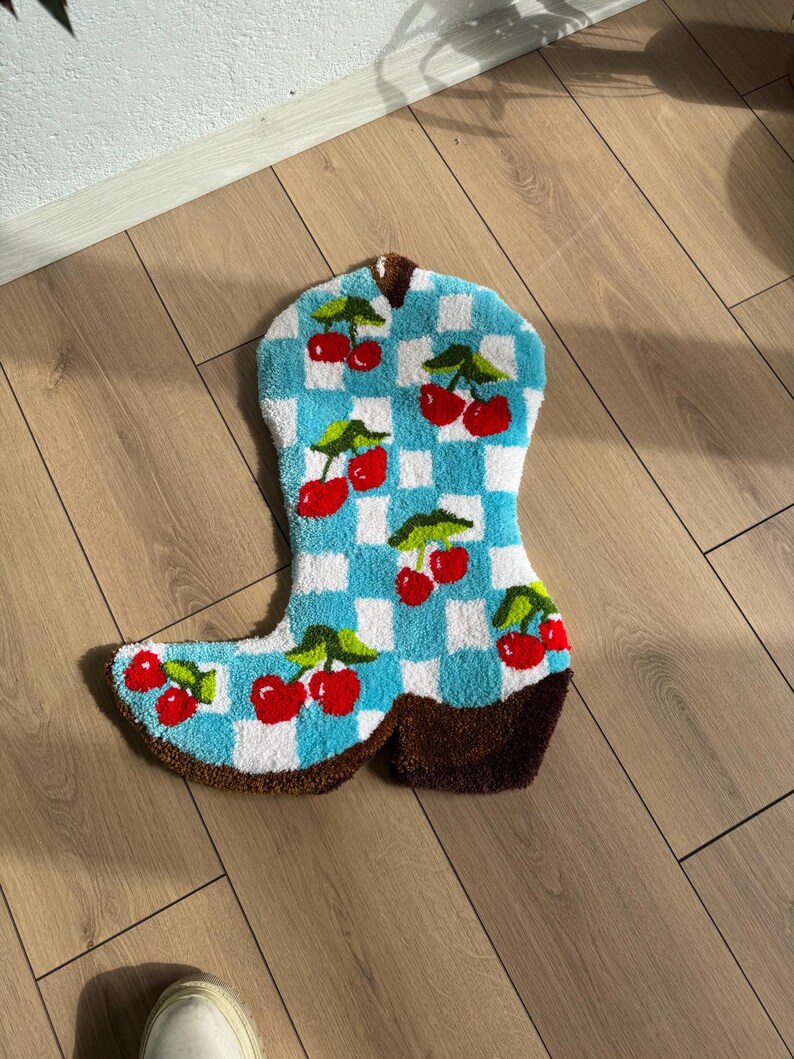 May include: A blue and white checkered boot rug with red cherries. The rug is made of a soft, fluffy material and has a brown leather-like heel.