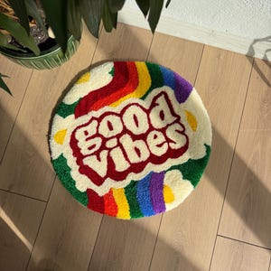 May include: Round, white, fluffy rug with a rainbow border and the words "Good Vibes" in red.