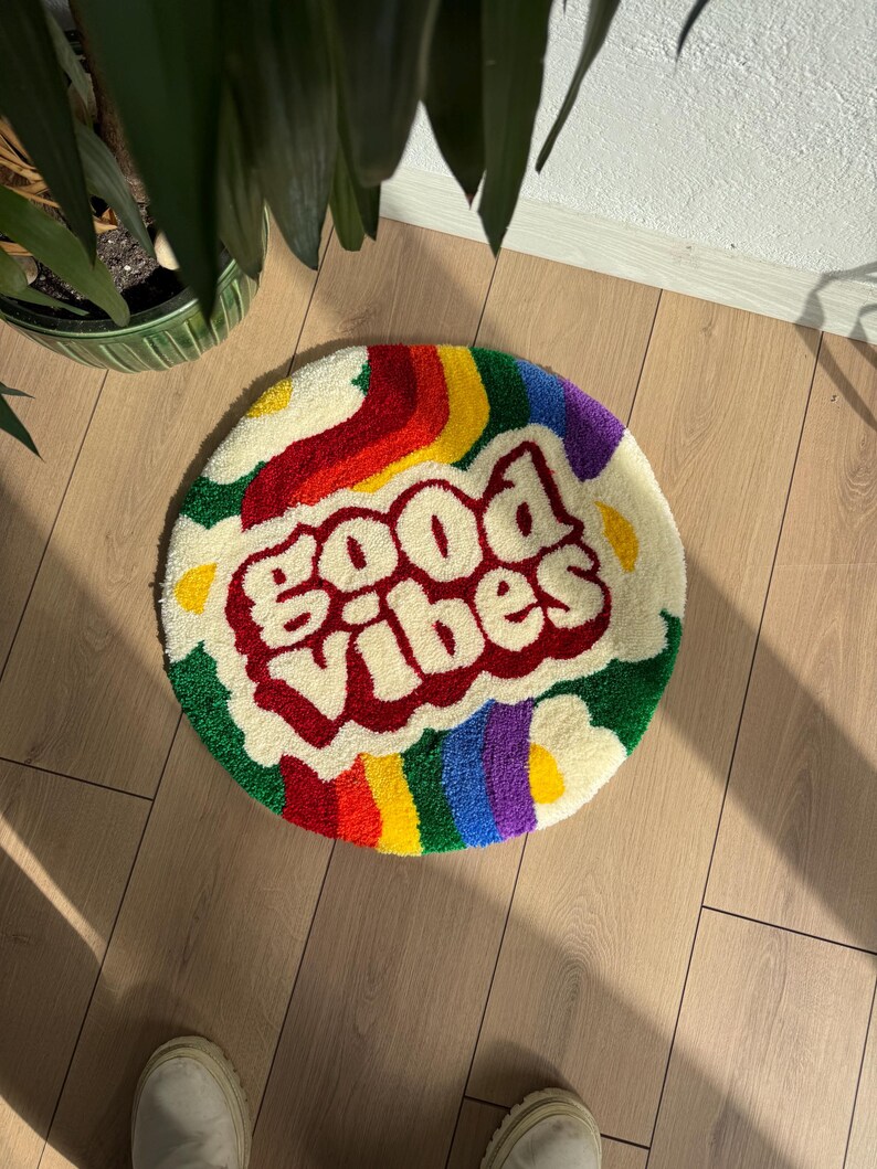 May include: Round, white, fluffy rug with a rainbow border and the words "Good Vibes" in red.