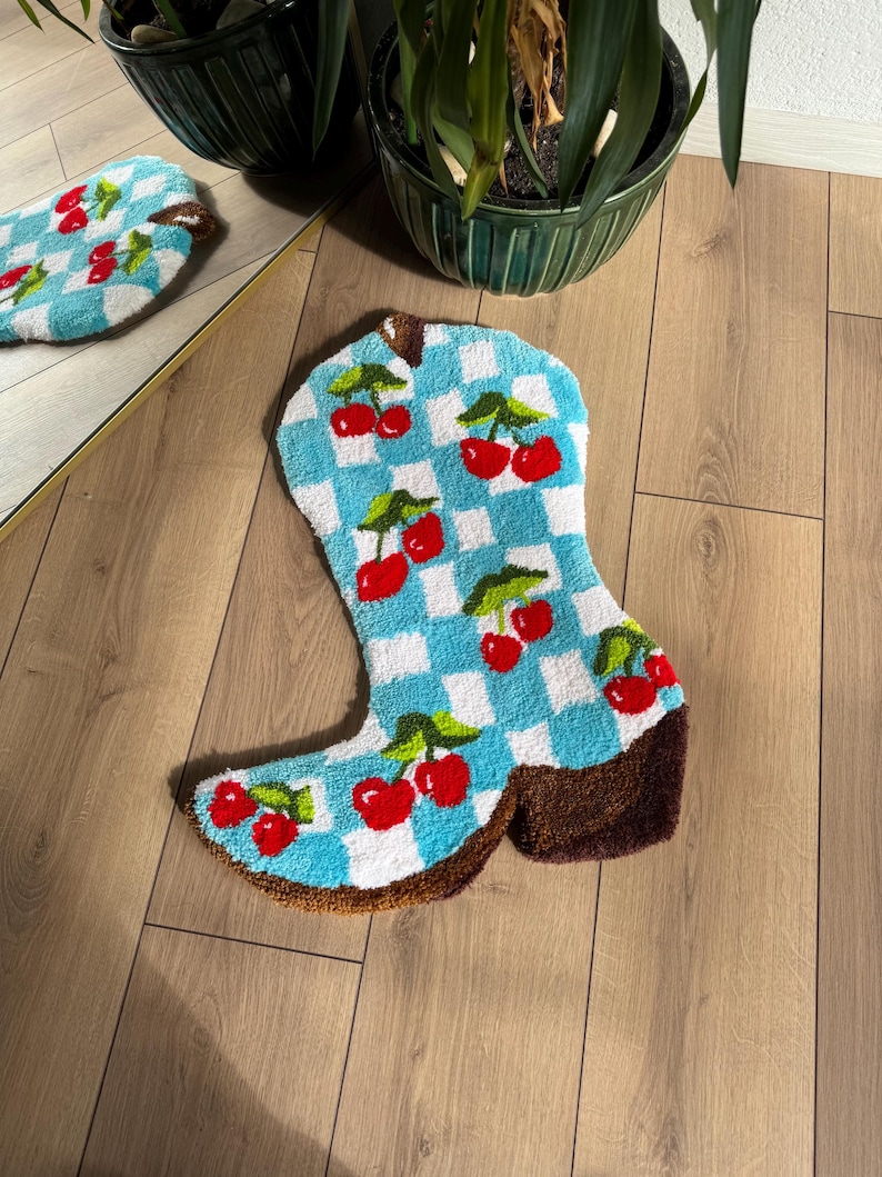 May include: A blue and white checkered boot-shaped rug with red cherries embroidered on it. The rug is on a wooden floor.