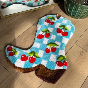 May include: A blue and white checkered rug shaped like a cowboy boot with red cherries embroidered on it.