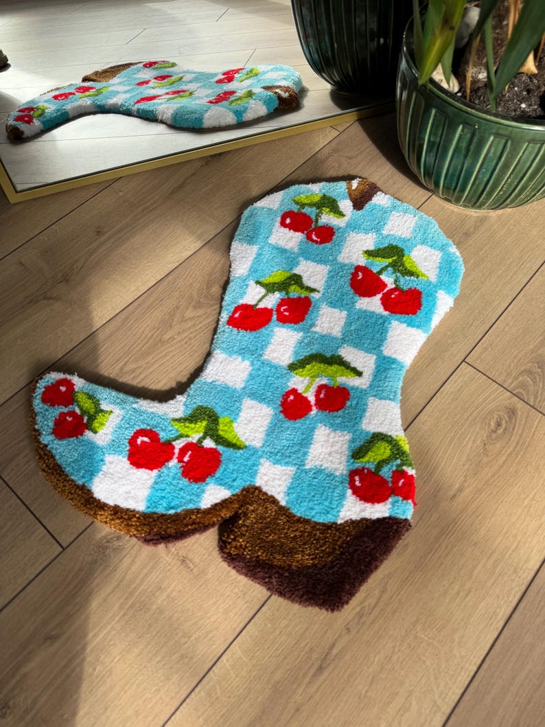 May include: A blue and white checkered rug shaped like a cowboy boot with red cherries embroidered on it.