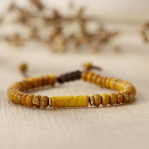 Op de afbeelding: Een gele kralen armband met een grotere gele stenen kraal in het midden. De armband is vastgebonden met een bruin koord.
