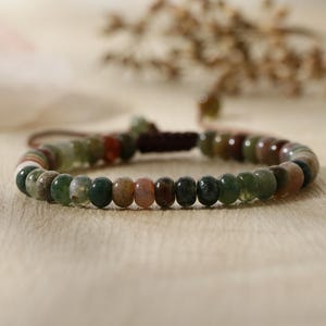 May include: A beaded bracelet with green, brown, and pink stones. The bracelet is made with a brown cord and has a knot closure.