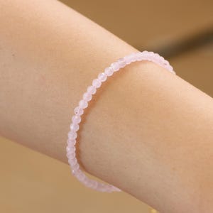 Puede incluir: Un delicado brazalete rosa hecho de pequeñas cuentas redondas. El brazalete se lleva en la muñeca.