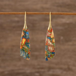 May include: A pair of gold-colored drop earrings. Each earring features a colorful, mosaic-like stone in shades of blue, green, yellow, and red. The earrings are suspended from a gold-colored hook.