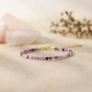 May include: A delicate purple gemstone bracelet with gold accents. The bracelet is made with small, faceted beads and has a simple, elegant design.