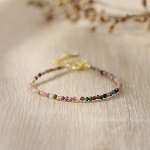 May include: A delicate bracelet made with small, colorful gemstones. The bracelet features a variety of colors, including pink, green, and white. The bracelet is made with a gold-toned clasp.
