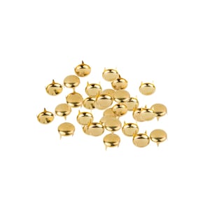 May include: A collection of small, shiny gold upholstery tacks. Each tack has a rounded head and a short, pointed pin. The tacks are scattered against a plain white background, creating a simple, clean aesthetic.