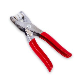 Pode incluir: Uma ferramenta de metal prateado com alças vermelhas para colocar ilhós e botões de pressão. A ferramenta tem uma alavanca e um conjunto de rolos para colocar os prendedores.