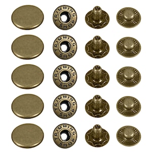 May include: Five sets of antique brass metal snap fasteners arranged in four columns. Each set includes a smooth round cap, a socket piece embossed with the text TRIMMING SHOP, a post, and a stud piece with a radial grooved pattern on the base.