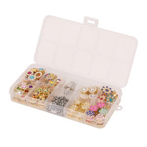 May include: A clear plastic storage container with ten compartments filled with various gold-toned metal embellishments featuring colorful embedded rhinestones in floral and star shapes, alongside a small silver metal tool component.