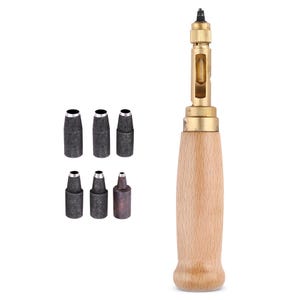 May include: A leather punch tool featuring a light-coloured wooden handle and a brass metal shaft with a small window. The set includes six interchangeable dark grey metal punch tips of varying sizes arranged in two rows to the left of the tool.