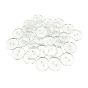 Può includere: Una collezione di numerosi bottoni circolari trasparenti, ciascuno dotato di due piccoli fori al centro. Queste chiusure rotonde e trasparenti sono disposte in un mucchio sparso, mettendo in risalto la loro superficie liscia e lucida e il design uniforme.