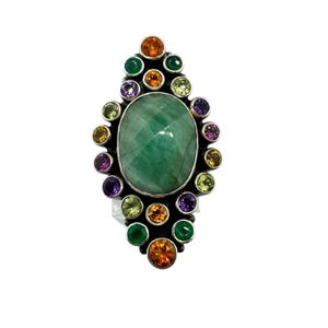 May include: A silver ring featuring a large, oval-cut, emerald-green gemstone at the center, surrounded by a halo of smaller, colorful gemstones. The accent stones include shades of orange, green, yellow, and purple. The ring has a detailed, ornate design.