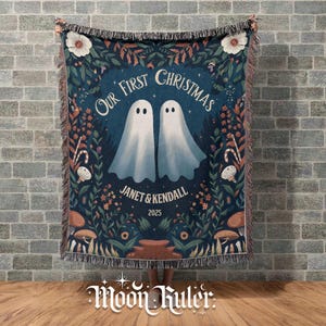 May include: A navy blue woven throw blanket with a whimsical design. The blanket features two ghost figures, the text "Our First Christmas", and the names "Janet & Kendall 2025". The design includes floral and mushroom elements.