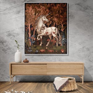May include: A framed wall art print featuring a white unicorn standing in a dense forest with dark red and brown foliage, surrounded by various flowers and plants. The artwork is displayed above a light wood media console with horizontal slats.