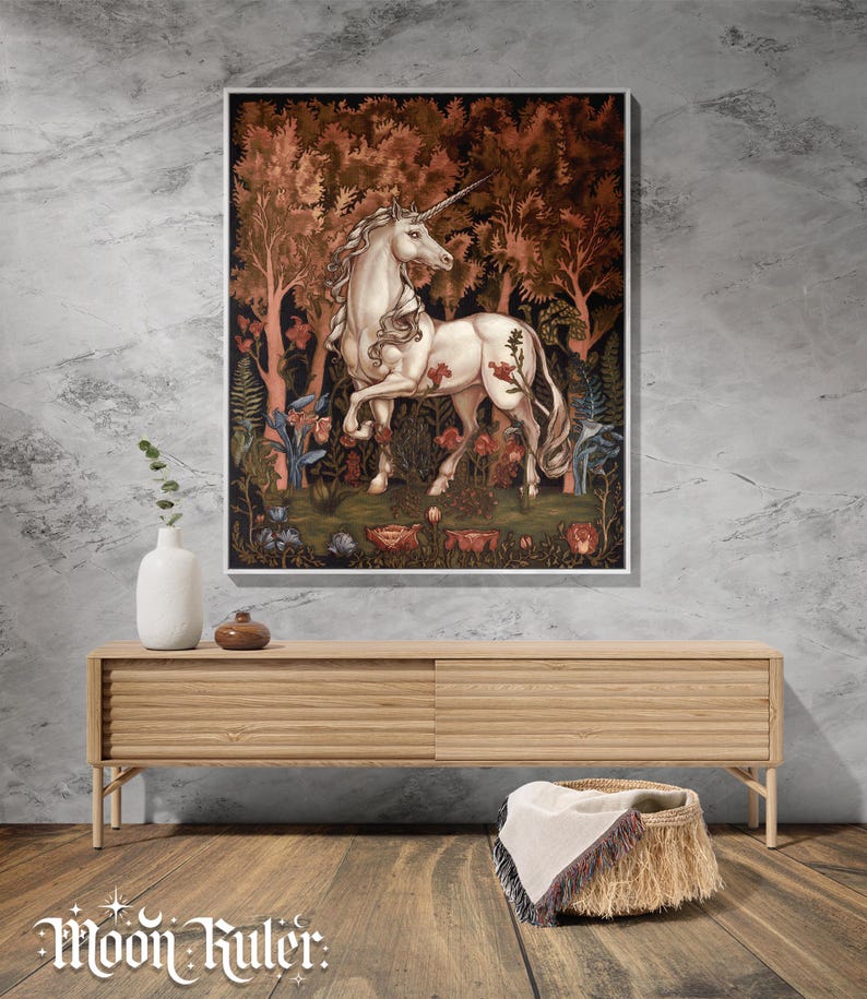 May include: A framed wall art print featuring a white unicorn standing in a dense forest with dark red and brown foliage, surrounded by various flowers and plants. The artwork is displayed above a light wood media console with horizontal slats.