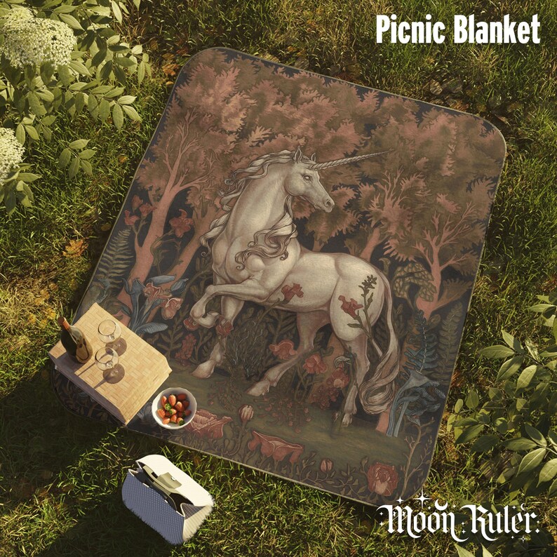 May include: A rectangular picnic blanket featuring a detailed illustration of a white unicorn standing in a forest with trees and flowers. The blanket has rounded corners and displays the text Picnic Blanket and Moon Ruler.