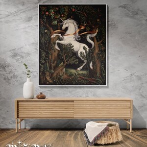 May include: A framed rectangular wall art print featuring a white unicorn standing in a dark, dense forest with green foliage and red fruit. The unicorn has a long horn and a flowing mane, with a gold ribbon draped across its body. The art is displayed.