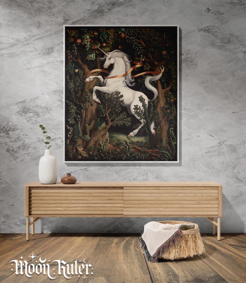 May include: A framed rectangular wall art print featuring a white unicorn standing in a dark, dense forest with green foliage and red fruit. The unicorn has a long horn and a flowing mane, with a gold ribbon draped across its body. The art is displayed.