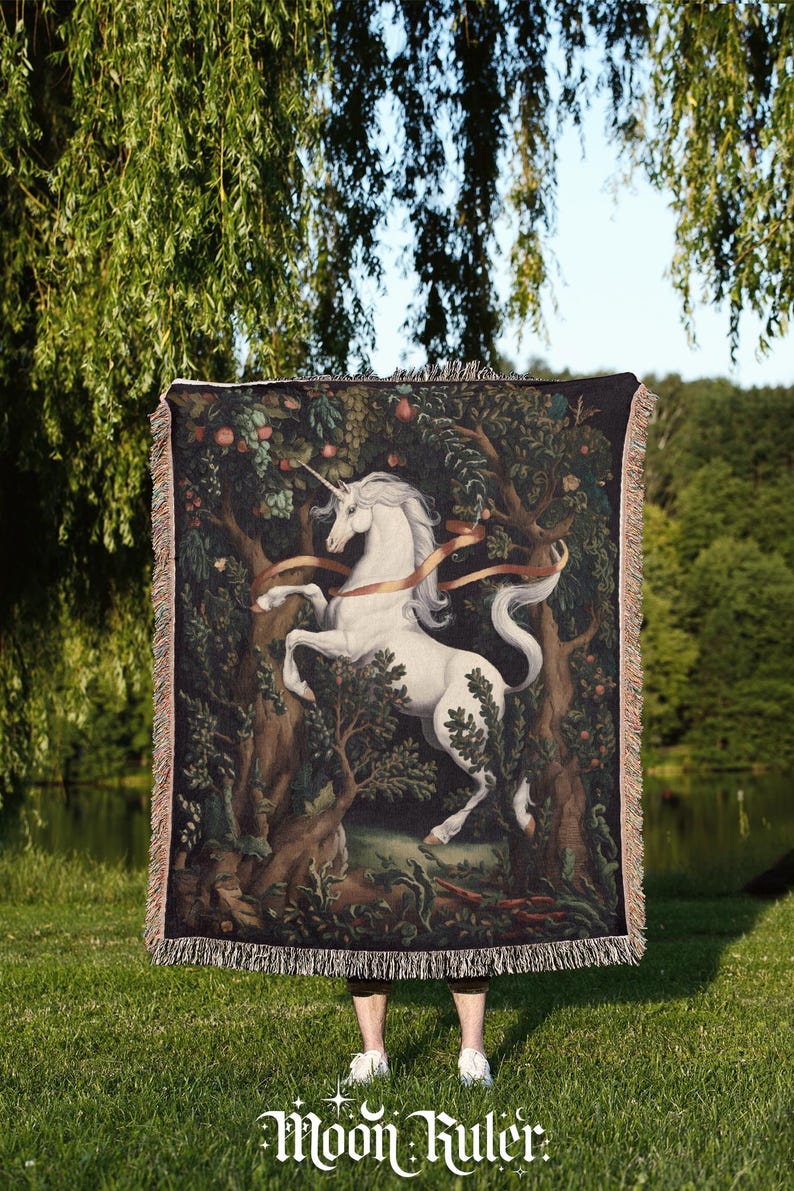 May include: A rectangular woven throw blanket featuring a white unicorn standing in a dark forest with trees, fruit, and a flowing ribbon. The blanket has a fringed edge on all sides and displays the text Moon Ruler at the bottom center.