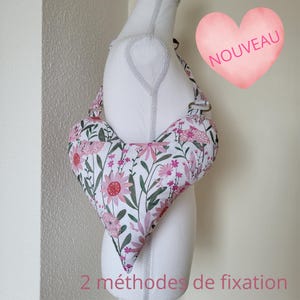 Peut inclure: Un sac en forme de cœur avec un tissu blanc à motif floral composé de fleurs roses et de feuilles vertes. Le sac comporte des anneaux métalliques pour les sangles et le texte NOUVEAU et 2 méthodes de fixation.
