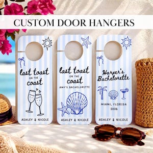 May include: Three rectangular door hangers with a light blue and white vertical striped pattern. Each features a circular cutout at the top and blue ink illustrations including suns, starfish, seashells, palm trees, and champagne flutes with text.