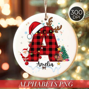 Puede incluir: Adorno navideño redondo con la letra "A" a cuadros rojos y negros, adornado con un gorro de Papá Noel y cuernos de reno. El diseño incluye un árbol de Navidad, Papá Noel y el nombre "Amelia". El texto "ALPHABETS PNG" está en la parte inferior.