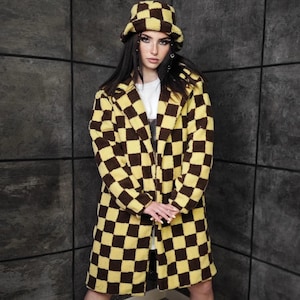 May include: A long coat and matching bucket hat in a yellow and brown checkerboard pattern. The coat has a collared neckline and falls to mid-calf. The hat is a classic bucket style. The outfit is paired with black boots.