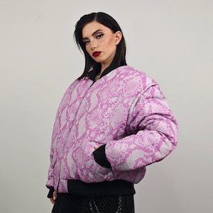 Könnte beinhalten: Eine rosafarbene und weiße Bomberjacke mit Schlangenmuster, schwarzem Reißverschluss und schwarzem Rippenbesatz.