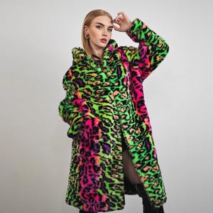 Könnte beinhalten: Ein langer Kapuzenmantel aus Kunstfell mit einem auffälligen Leopardenmuster in Neon-Grün, Pink und Lila. Der Mantel hat eine lockere Passform und ist knielang. Die Ärmel sind lang und der Mantel ist vorne offen.