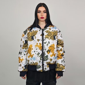 Peut inclure: Une veste bomber blanche avec un imprimé floral abstrait coloré. La veste a une fermeture éclair et un col, des poignets et une ourlet côtelés.