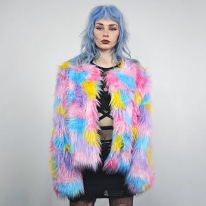 May include: A vibrant faux fur jacket in a patchwork design. The jacket features a mix of pink, blue, yellow, and purple hues. The jacket is open-fronted and has long sleeves. The model is wearing a black top and skirt.
