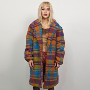 Könnte beinhalten: Ein langer, farbenfroher karierter Mantel in Orange-, Blau-, Lila- und Grüntönen. Der Mantel hat ein flauschiges, strukturiertes Aussehen und einen breiten Kragen. Der Mantel ist knielang und scheint aus einem weichen, warmen Material zu sein.