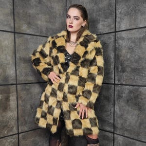 Può includere: Un lungo cappotto in ecopelliccia con motivo a scacchiera nei toni del beige e del marrone scuro. Il cappotto ha un colletto classico e un taglio al ginocchio. La modella indossa un top nero con paillettes e calze nere.