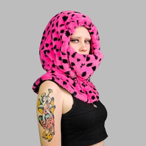 Op de afbeelding: Een roze en zwarte luipaardprint balaclava met een ritssluiting. De balaclava is gemaakt van een zacht, pluche materiaal en bedekt het hoofd en de nek.