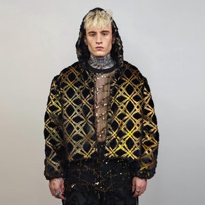 May include: A black and gold patterned jacket with a hood. The jacket features a geometric design and is made from a soft, plush fabric.
