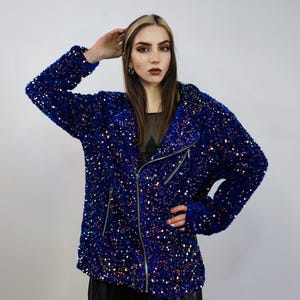 Puede incluir: Chaqueta azul brillante con lentejuelas y cierre de cremallera plateada. La chaqueta tiene un estilo motero clásico con cuello con solapas y mangas largas. Las lentejuelas crean un efecto brillante.