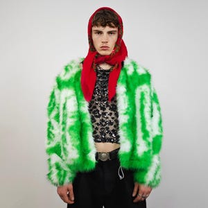 May include: A striking green and white faux fur jacket. The jacket features a bold pattern and a cropped design. The model is wearing a red headscarf and a black sequined top. The outfit is completed with black trousers and a silver belt, creating a bold fashion statement.