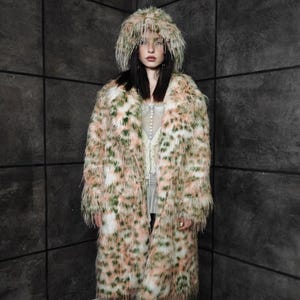 May include: A long faux fur coat and matching hat. The coat features a spotted pattern in white, peach, and green. The coat has a wide collar and reaches the ankles. The hat is a close-fitting style with a feathered trim. A bold fashion statement.