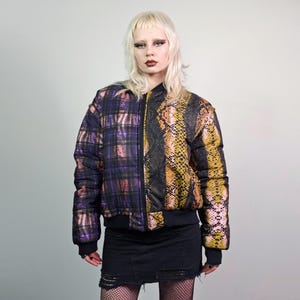 May include: A black bomber jacket with a purple and black plaid pattern on one side and a brown and yellow snake print on the other side.