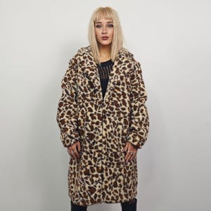 Puede incluir: Abrigo largo de piel sintética con estampado de leopardo en tonos marrón y crema. El abrigo tiene un cuello clásico y una botonadura frontal. El abrigo es hasta la rodilla y tiene mangas largas.