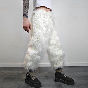 May include: White faux fur pants with a shaggy texture. The pants have a wide leg design and are paired with black platform boots. The outfit is completed with a white tank top.