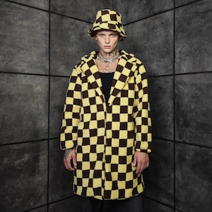 May include: A yellow and brown checkered coat and matching bucket hat. The coat is long with a hood and a checkered pattern. The hat is also checkered. The person is wearing a black shirt and a silver necklace.