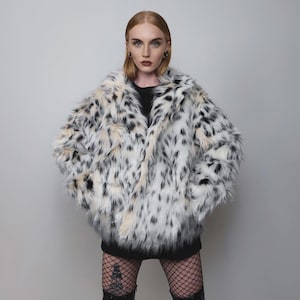 May include: A faux fur coat with a spotted pattern in black, white, and tan. The coat has a wide collar and a loose fit. The coat is a statement piece, perfect for adding a touch of glamour to any outfit.
