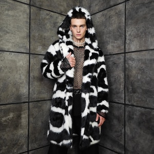 May include: A long, hooded coat featuring a black and white cow print design. The coat is open, showing a black mesh top. The model is wearing black trousers and a silver chain necklace.